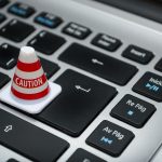 a miniature traffic cone labeled "caution" sitting on a computer keyboard